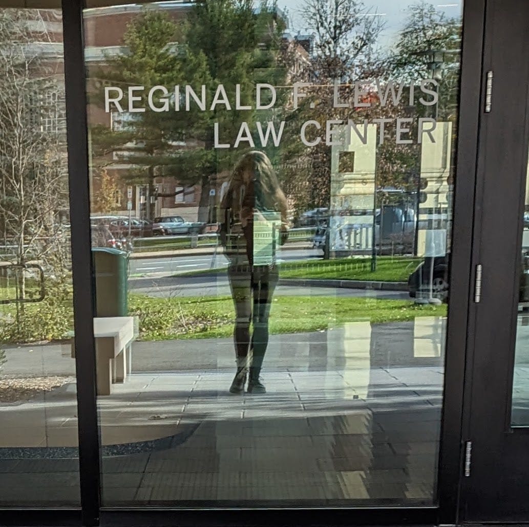 Molly White, reflected in the glass door of the Reginald F. Lewis Law Center on the Harvard campus