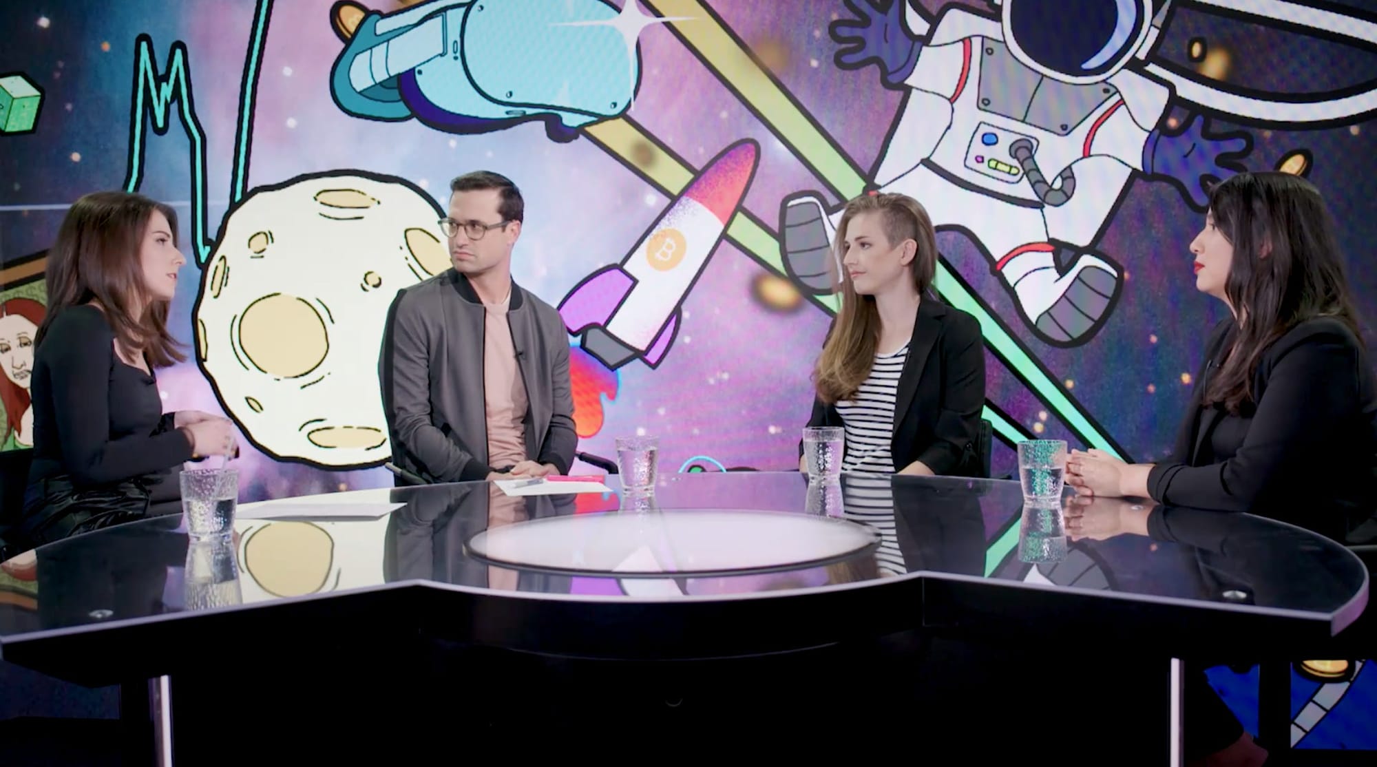 Katie Greifeld, Tim Stenovic, Molly White, and Tonantzin Carmona sit around a semicircular table in front of a backdrop with a space background, covered with cartoonish illustrations of rockets, moons, and crypto charts