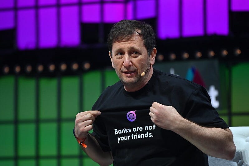 Alex Mashinsky on a stage, displaying a shirt he is wearing with the Celsius logo that says "Banks are not your friends"