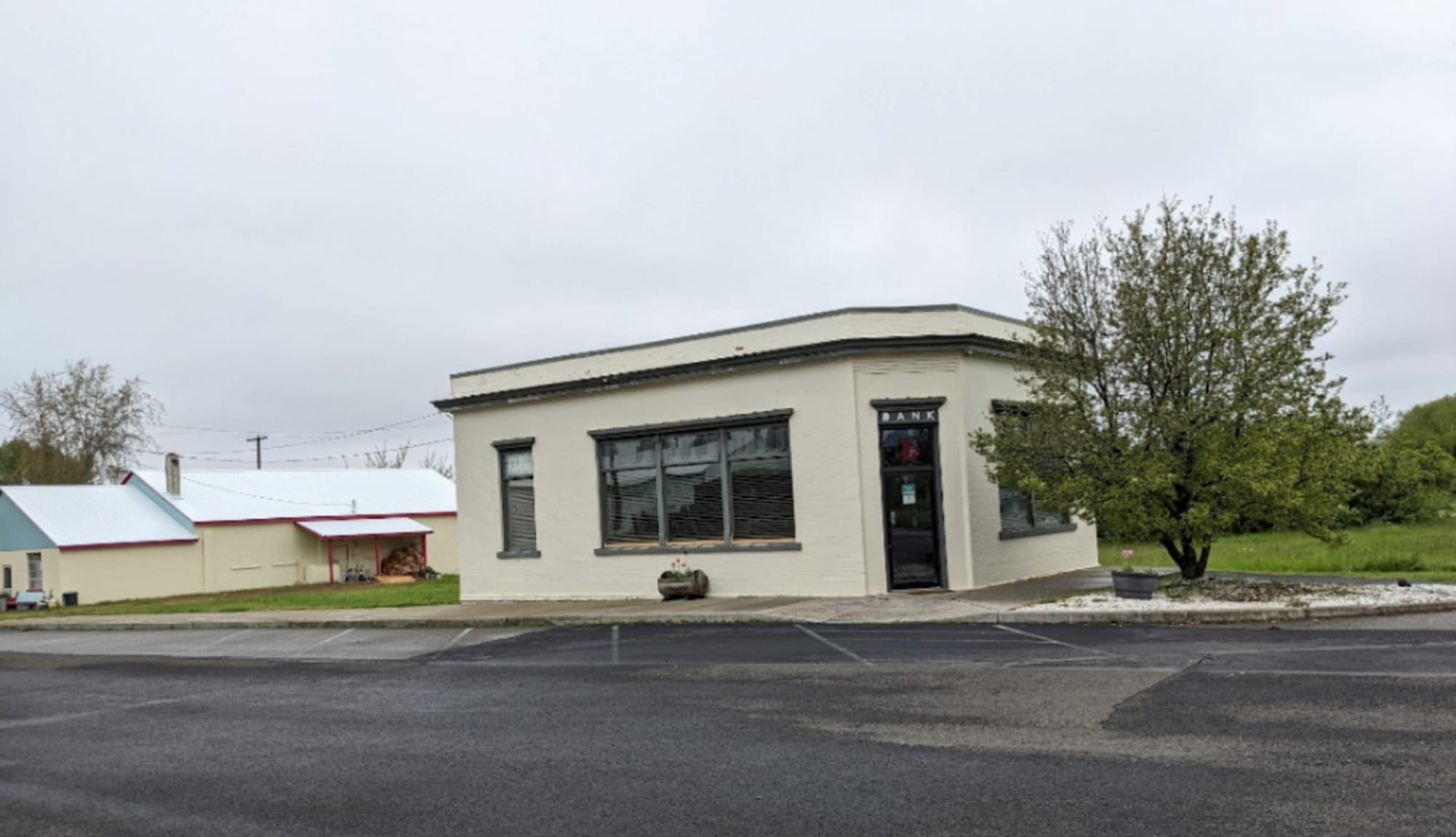 Photograph of a small, boxy, white brick or cement building. The word "BANK" is visible above the door.