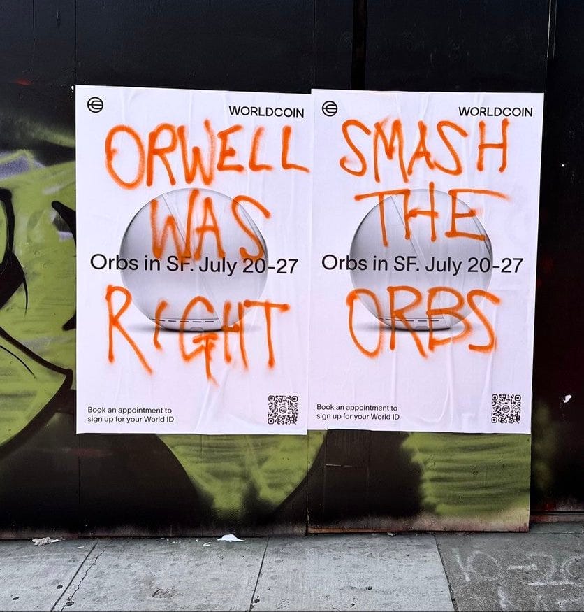 Graffiti on Worldcoin posters in San Francisco, reading "Orwell was right, smash the orbs" in orange spray paint