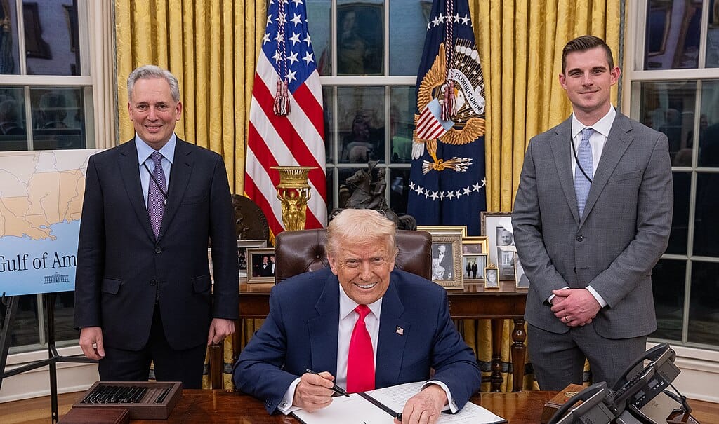 David Sacks, Donald Trump, and Bo Hines pose for a photo in the Oval Office. Trump is seated at the Resolute Desk, the others stand to either side.