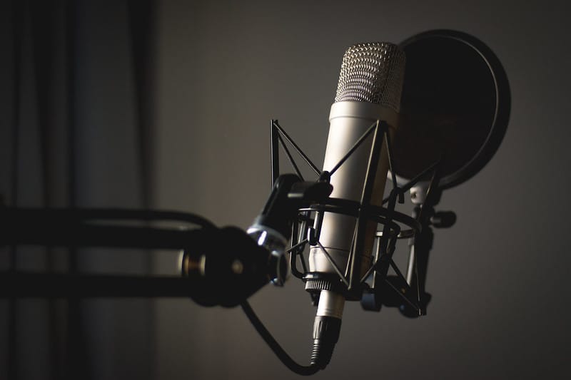 A podcasting microphone with a pop filter and shock mount, mounted on a microphone arm
