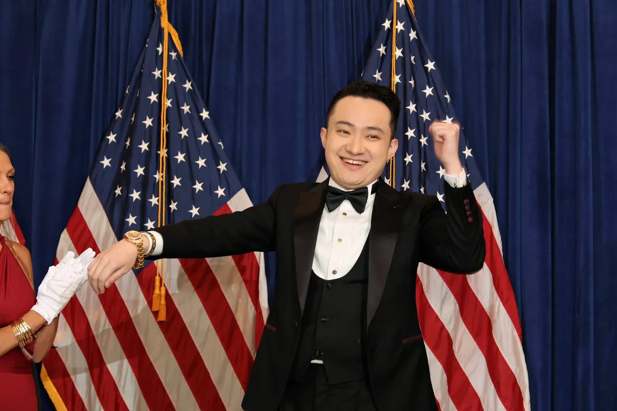 Justin Sun displays his Trump Watch at the first memecoin dinner, where he stands in front of two American flags