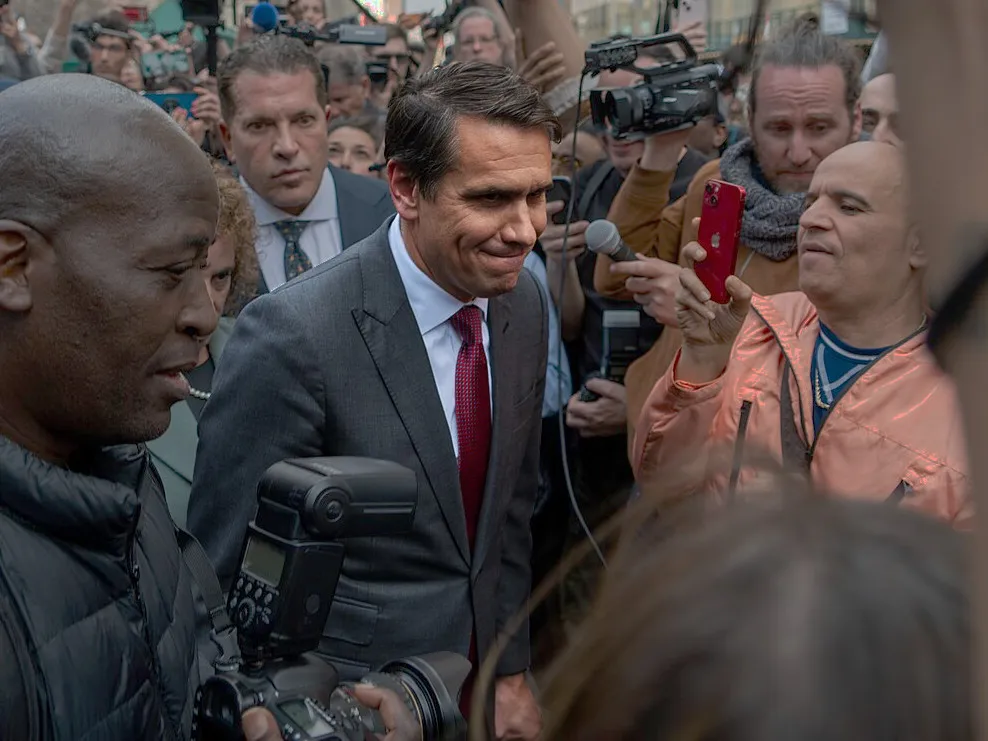Todd Blanche wearing a suit amid a throng of reporters