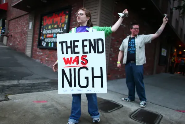 A person stands with a sandwich board on their shoulders saying "The end WAS nigh". 