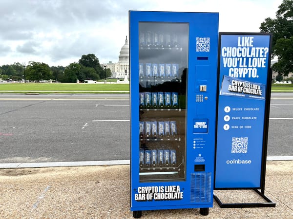 A blue vending machine with branding that reads “Crypto is like a bar of chocolate” in the foreground, with the Capitol building behind