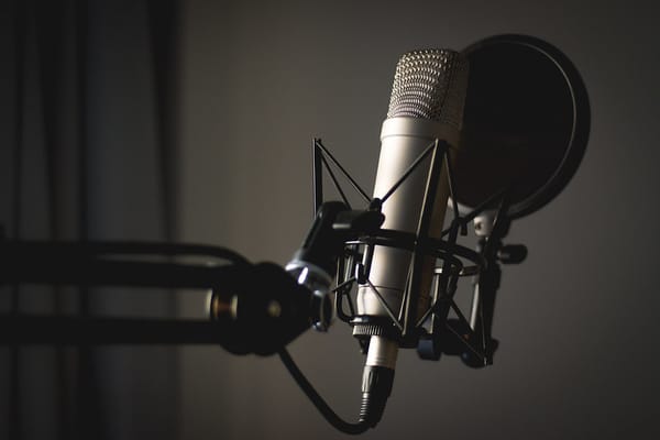 A podcasting microphone with a pop filter and shock mount, mounted on a microphone arm