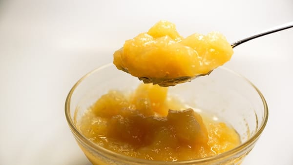 A spoon lifting a spoonful of applesauce from a glass bowl
